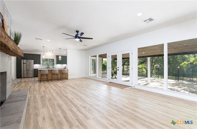 unfurnished living room with french doors, light hardwood / wood-style floors, ceiling fan, and sink