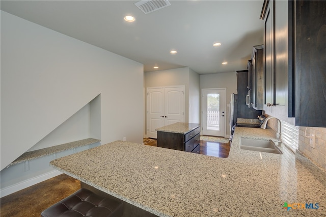 kitchen with sink, a center island, backsplash, and light stone countertops