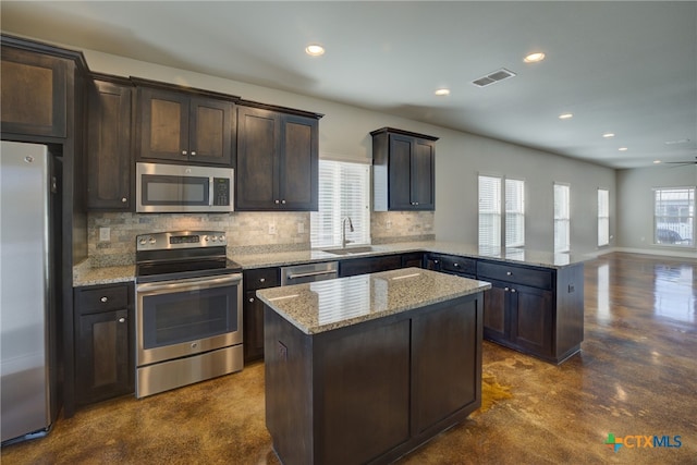 kitchen featuring stainless steel appliances, light stone counters, a center island, and plenty of natural light