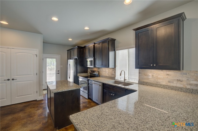 kitchen with a kitchen island, light stone countertops, appliances with stainless steel finishes, and sink