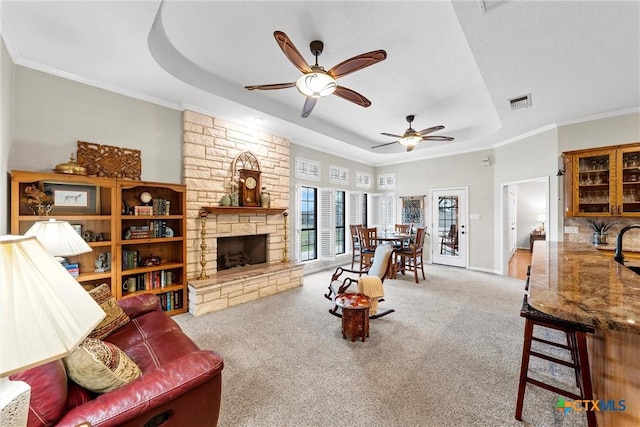 carpeted living room with ceiling fan, ornamental molding, a fireplace, and a raised ceiling