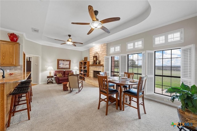 carpeted dining room with ornamental molding, a healthy amount of sunlight, a fireplace, and a raised ceiling