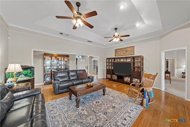 living room with crown molding, ceiling fan, wood-type flooring, and a tray ceiling