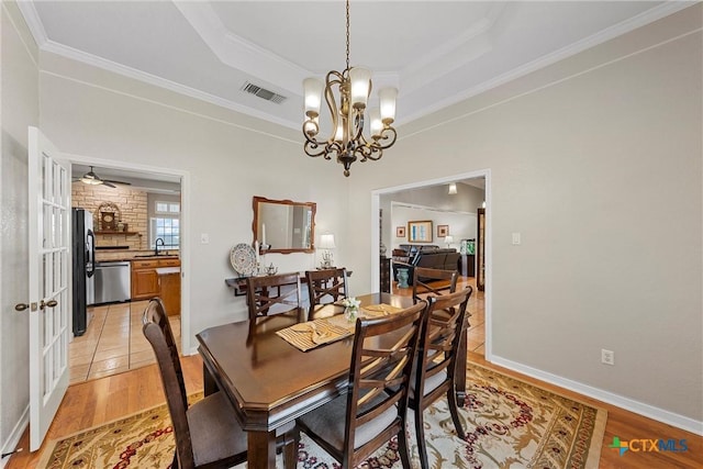 dining room with sink, light hardwood / wood-style flooring, a raised ceiling, and a chandelier