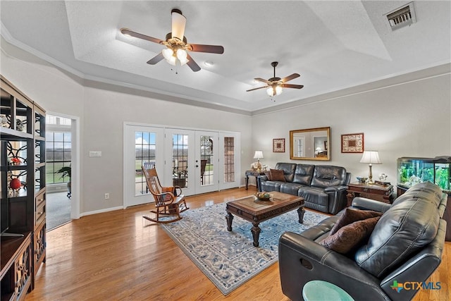 living room with light wood-type flooring, ceiling fan, a raised ceiling, a textured ceiling, and french doors