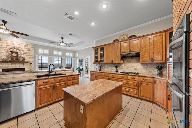 kitchen featuring sink, appliances with stainless steel finishes, a kitchen island, light stone countertops, and decorative backsplash