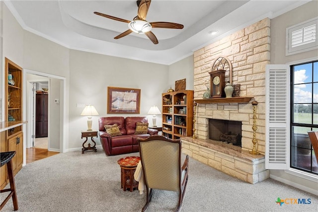 carpeted living room with crown molding, a fireplace, a tray ceiling, and ceiling fan