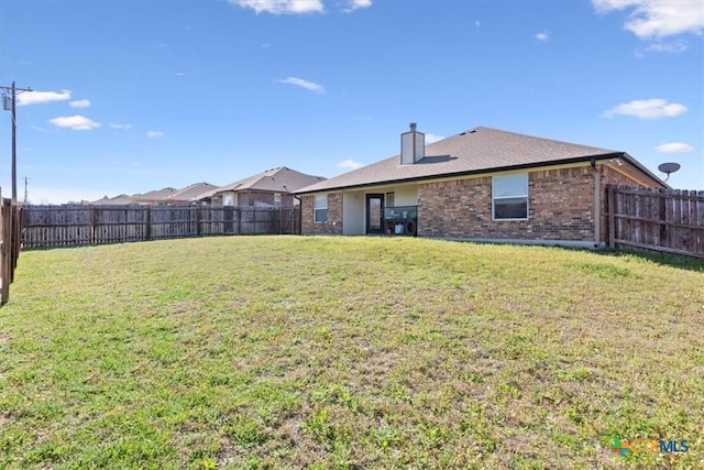 rear view of house with a lawn, brick siding, and a fenced backyard