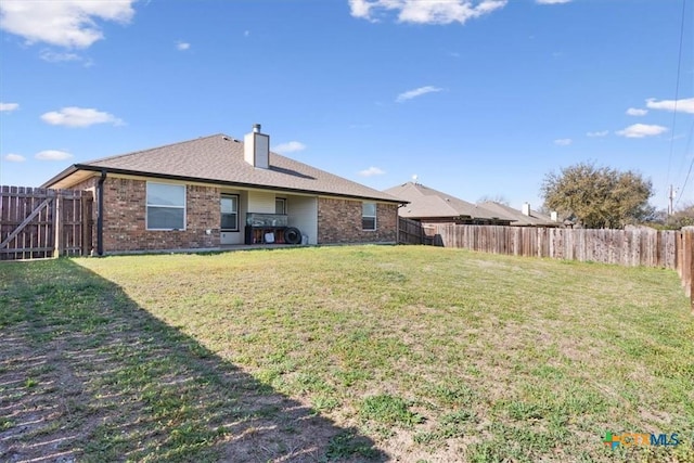 back of property featuring a yard, brick siding, a fenced backyard, and a chimney