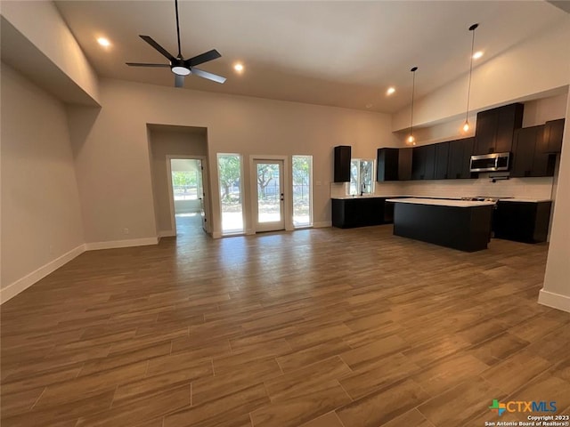 kitchen featuring stainless steel microwave, open floor plan, a center island, light countertops, and high vaulted ceiling