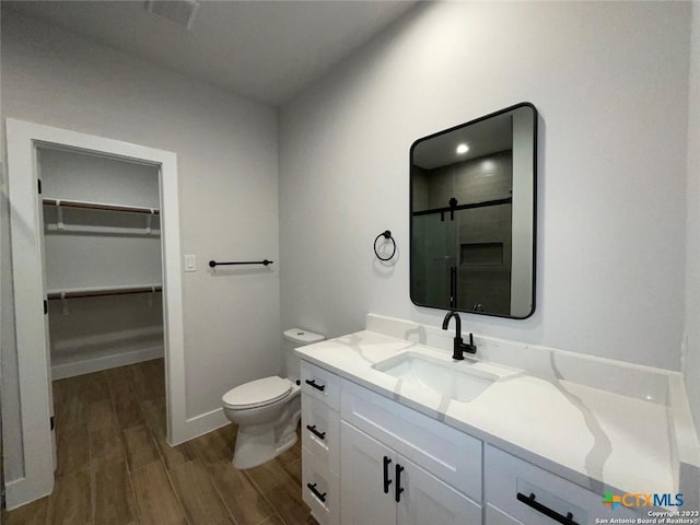 bathroom with a spacious closet, toilet, a stall shower, vanity, and wood finished floors