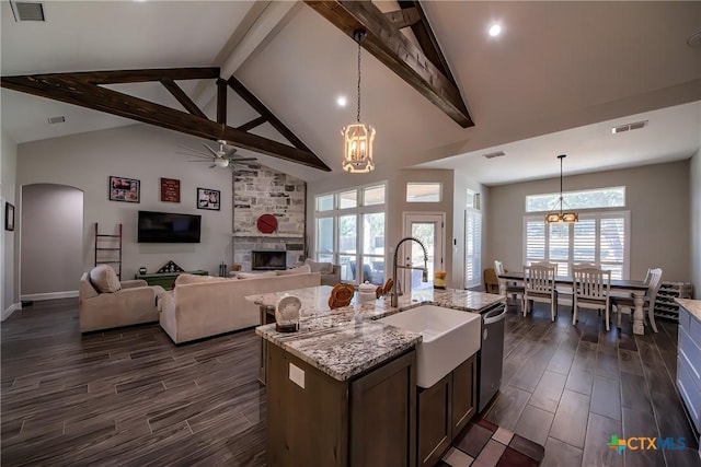 kitchen featuring pendant lighting, a center island with sink, sink, a fireplace, and beam ceiling