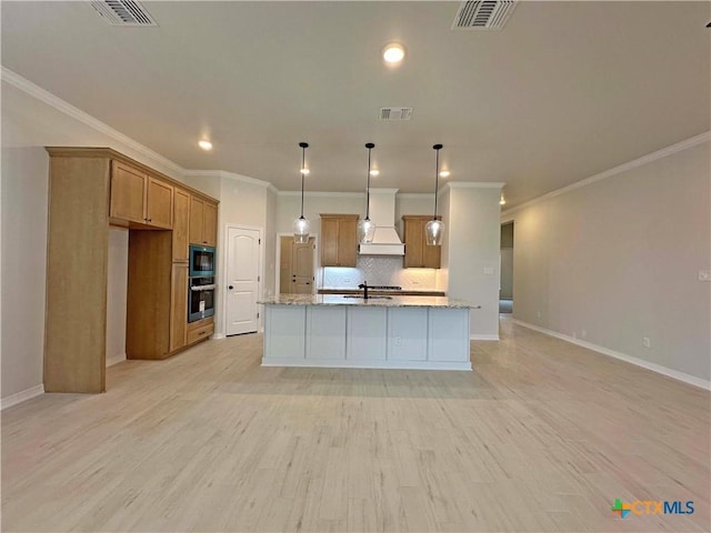 kitchen featuring custom exhaust hood, light stone counters, hanging light fixtures, a center island with sink, and backsplash