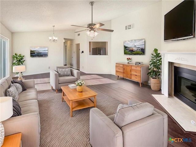 living room featuring ceiling fan with notable chandelier, dark wood-type flooring, and vaulted ceiling