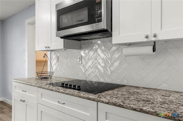 8704 Trailridge Dr, Temple, TX 76502 - kitchen featuring stainless steel microwave, black electric stovetop, white cabinets, and backsplash