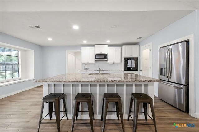 8704 Trailridge Dr, Temple, TX 76502 - kitchen featuring stainless steel appliances, wood finished floors, white cabinets, recessed lighting, and light stone counters