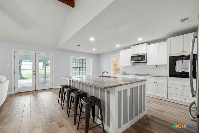 8704 Trailridge Dr, Temple, TX 76502 - kitchen featuring black appliances, light wood-style floors, an island with sink, light stone counters, and french doors