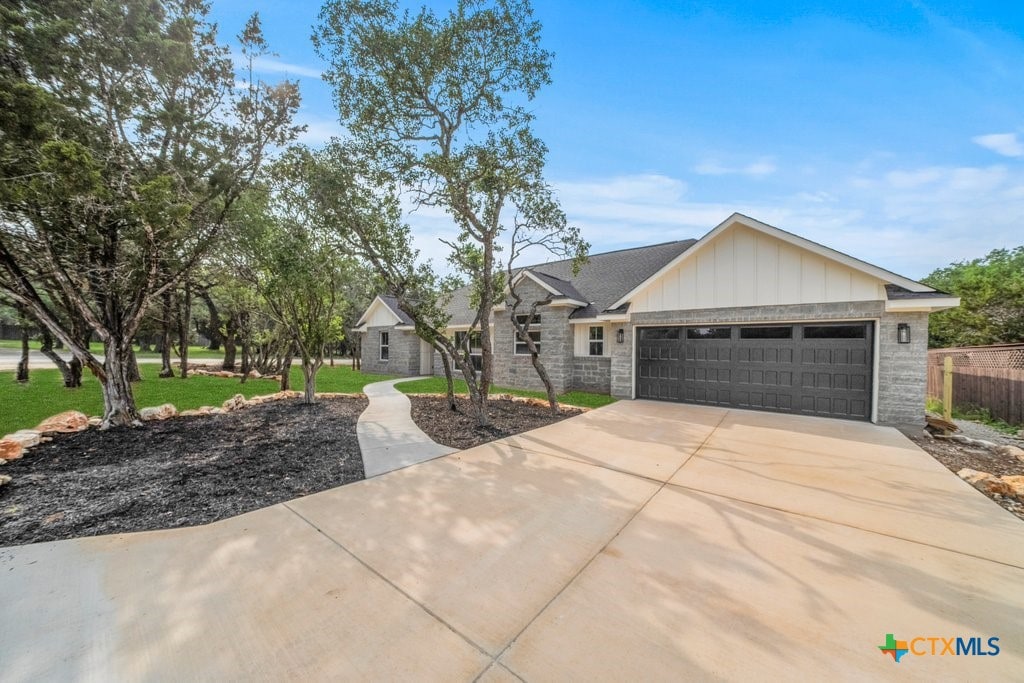 2 Stepping Stone Ct, Wimberley, TX 78676 - view of front facade with an attached garage, driveway, stone siding, and board and batten siding