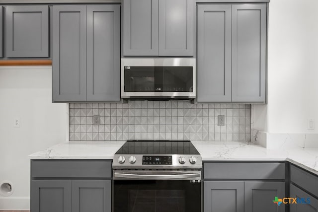 kitchen with gray cabinets, appliances with stainless steel finishes, decorative backsplash, and light stone counters