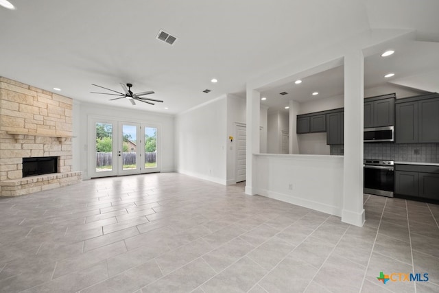 unfurnished living room with a stone fireplace, french doors, ornamental molding, ceiling fan, and light tile patterned flooring