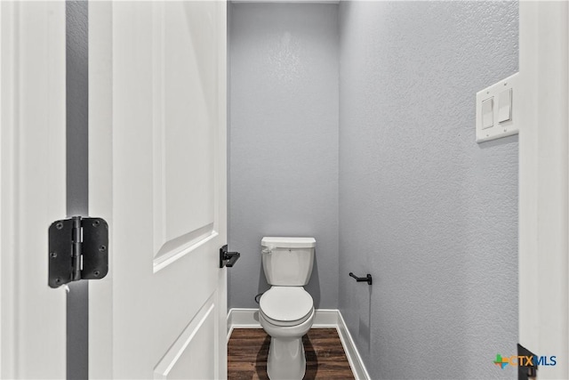 bathroom featuring toilet, baseboards, wood finished floors, and a textured wall