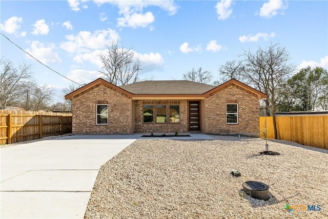 view of front of home featuring fence private yard, brick siding, and roof with shingles