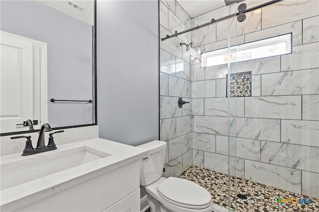 bathroom featuring visible vents, a textured wall, toilet, vanity, and a shower stall