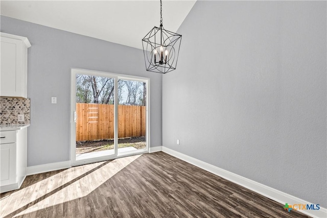 unfurnished dining area featuring baseboards, dark wood-style flooring, lofted ceiling, and an inviting chandelier