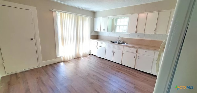 kitchen with white cabinets, a textured ceiling, sink, and light hardwood / wood-style flooring