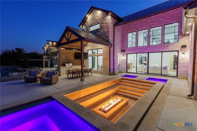 back house at twilight featuring an outdoor fire pit, a patio area, and exterior kitchen