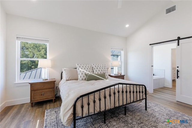 bedroom featuring hardwood / wood-style flooring, a barn door, connected bathroom, and vaulted ceiling