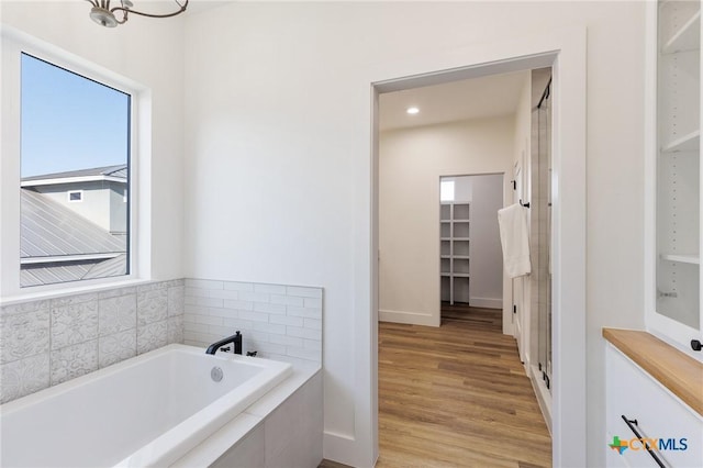 bathroom featuring hardwood / wood-style flooring, an inviting chandelier, and tiled tub