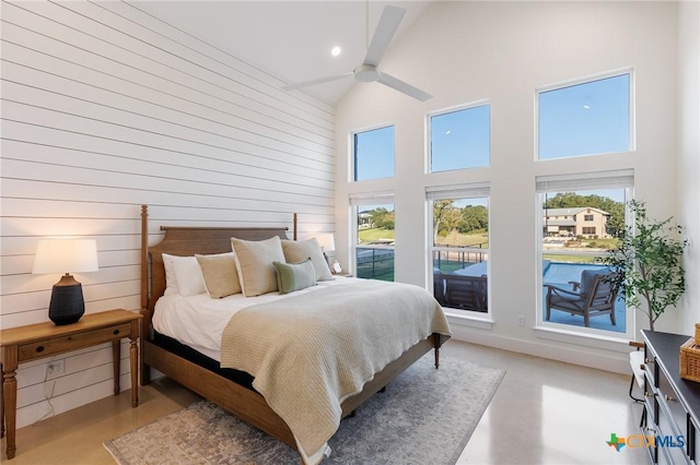 bedroom with ceiling fan, wood walls, and a high ceiling