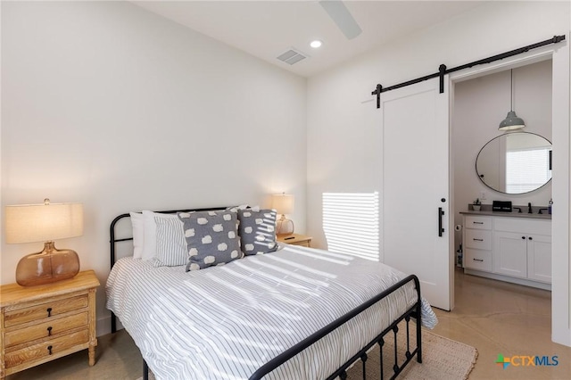 bedroom featuring ceiling fan, a barn door, light carpet, and connected bathroom