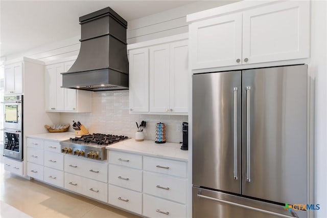 kitchen featuring white cabinetry, light stone countertops, tasteful backsplash, custom range hood, and appliances with stainless steel finishes