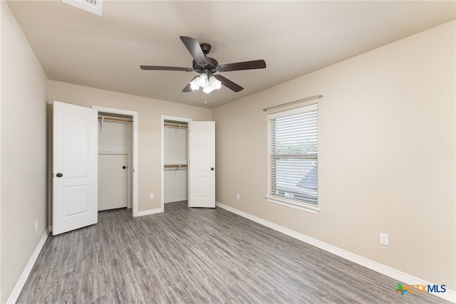 unfurnished bedroom featuring ceiling fan, multiple closets, and light hardwood / wood-style flooring