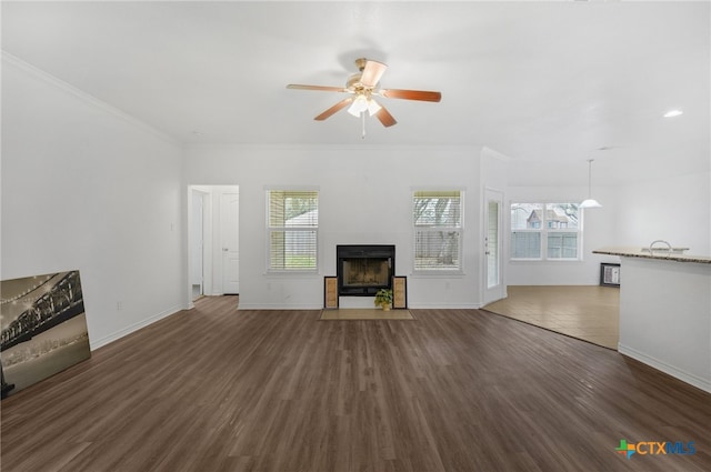 unfurnished living room featuring a tile fireplace, dark wood-type flooring, ceiling fan, and ornamental molding