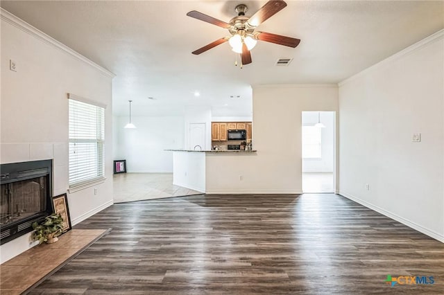 unfurnished living room with crown molding, ceiling fan, dark hardwood / wood-style flooring, and a tiled fireplace