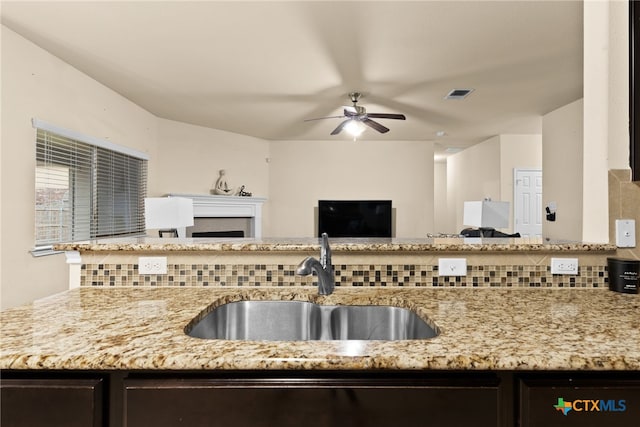 kitchen with decorative backsplash, light stone counters, ceiling fan, and sink