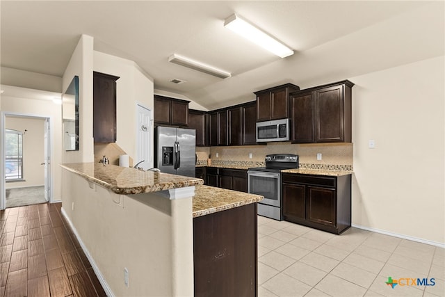 kitchen with light stone countertops, backsplash, kitchen peninsula, a breakfast bar area, and appliances with stainless steel finishes