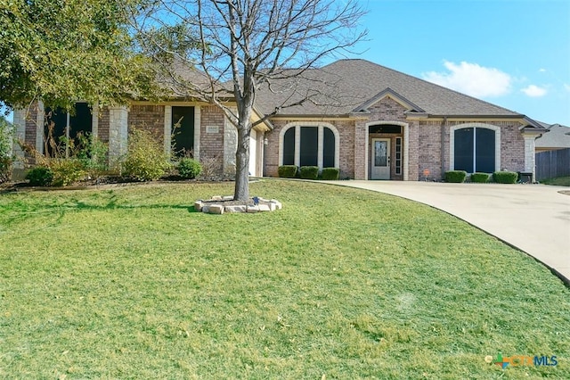 french country home featuring brick siding, roof with shingles, concrete driveway, and a front yard