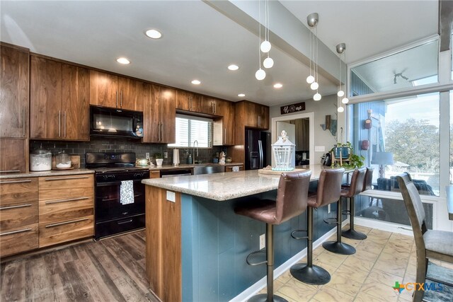 kitchen with a kitchen bar, light wood-type flooring, tasteful backsplash, black appliances, and a kitchen island