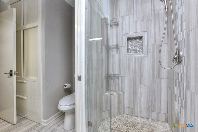 bathroom with hardwood / wood-style floors, toilet, and a tile shower