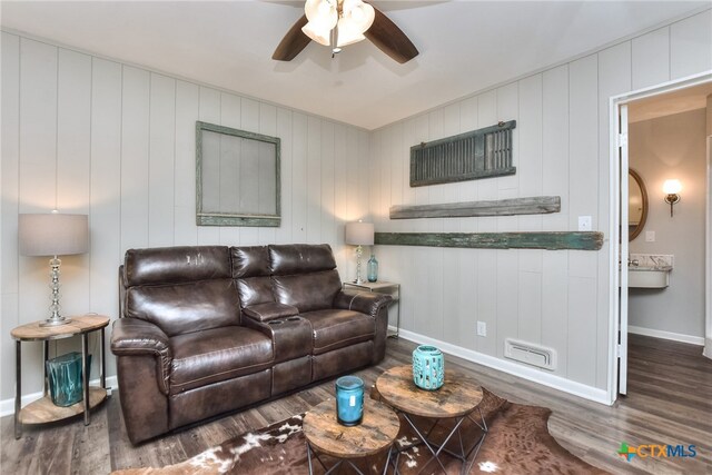 living room with ceiling fan, wooden walls, and dark wood-type flooring