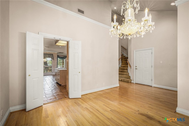 empty room with a high ceiling, light wood-type flooring, and ornamental molding