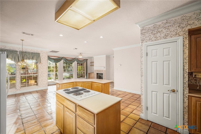 kitchen with crown molding, a kitchen island, white stovetop, a tiled fireplace, and ceiling fan