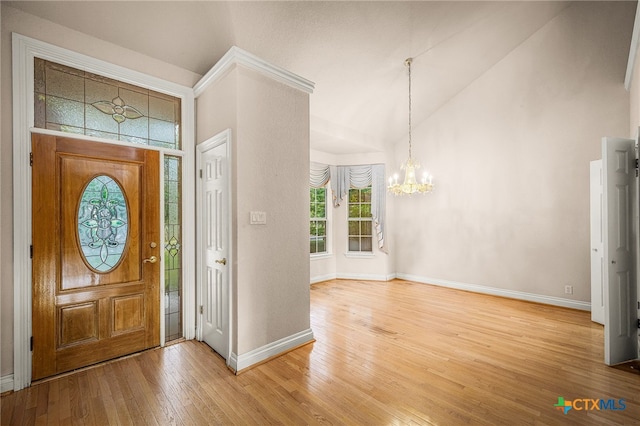 foyer entrance with wood-type flooring, a notable chandelier, and vaulted ceiling