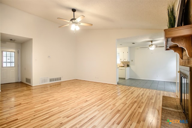 unfurnished living room with a fireplace, a textured ceiling, vaulted ceiling, ceiling fan, and light hardwood / wood-style flooring