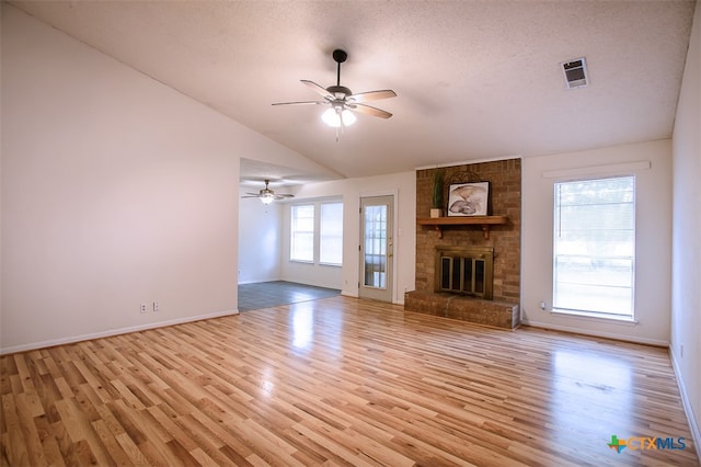 unfurnished living room with a brick fireplace, lofted ceiling, a textured ceiling, ceiling fan, and light wood-type flooring