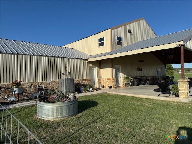 rear view of property with a yard, a patio, and stone siding